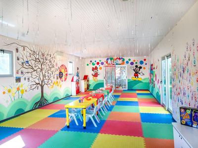 Barevná herna s stoly, židlemi a veselými malbami na stěnách pro děti.