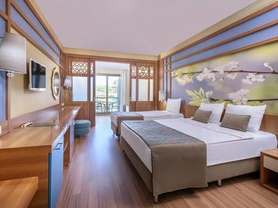 Světý hotelový pokoj se dvěma dvoulůžky, nástěnnou dekorací a výhledem na balkón.