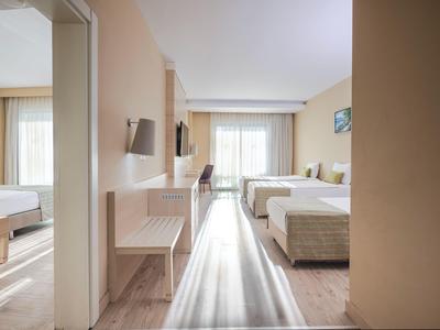 Pasillo luminoso del hotel con vista a dos camas individuales y una habitación contigua con cama doble.