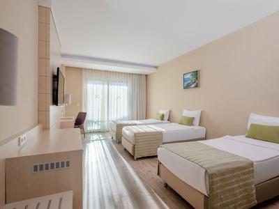 Habitación de hotel moderna con dos camas individuales, escritorio y balcón con suelo claro.