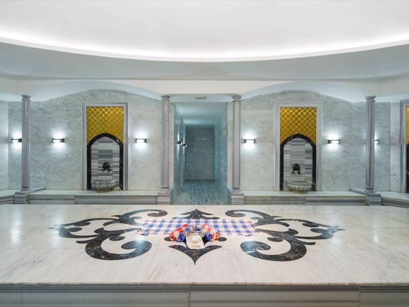Velký kruhový spa pokoj s mozaikovým vzorem na podlaze a mramorovými lavicemi podél stěn.