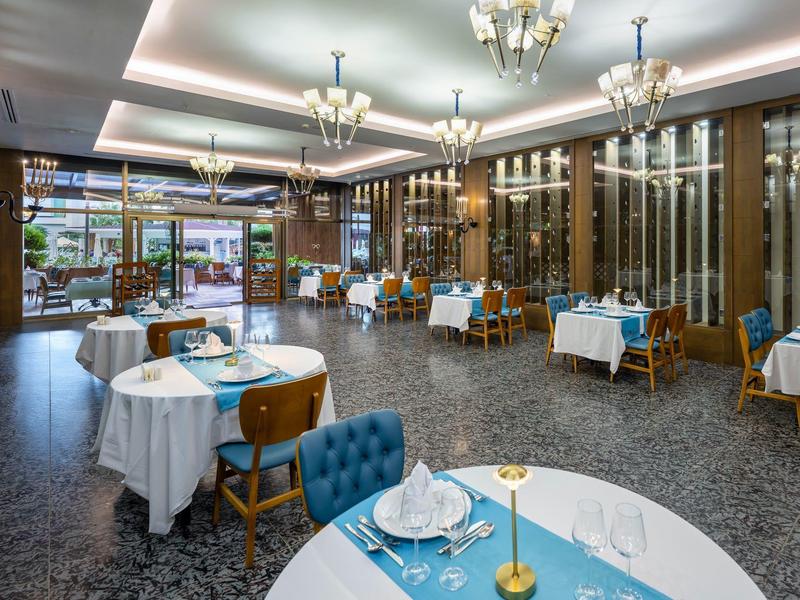Elegantní restaurace s kulatými stoly a modrými akcenty v luxusním prostředí.