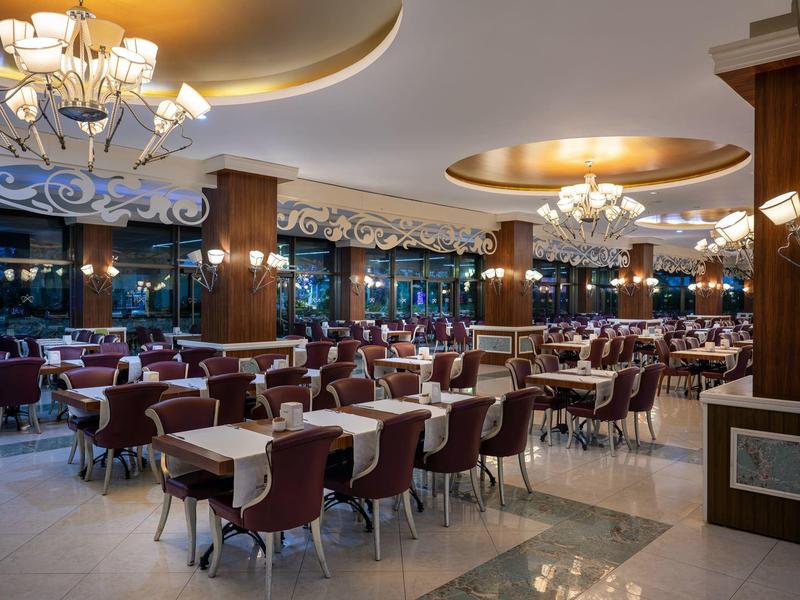 Elegantní, prostorná jídelna s mnoha stoly, židlemi a lustry.