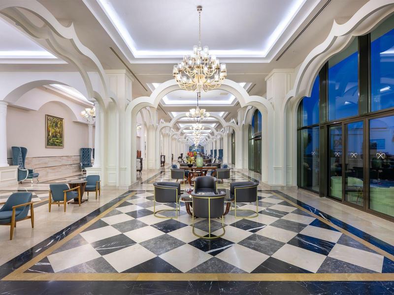 Elegantní hotelová lobby s černobílou šachovnicovou podlahou, lustry a velkými okny.