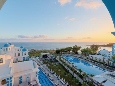 Vista di un resort con piscine, edifici bianchi e mare al tramonto.