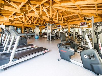 Palestra luminosa con varie attrezzature per l'allenamento e soffitto in legno visibile.