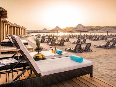 Sdraio con asciugamani blu e bevande sulla spiaggia sabbiosa al tramonto.