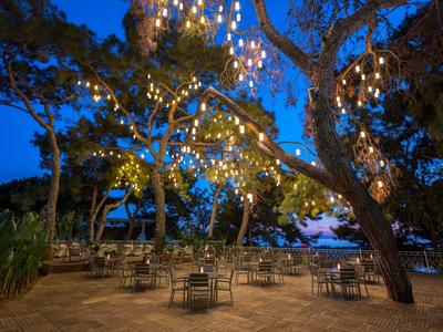 Area esterna illuminata con tavoli e sedie sotto gli alberi al crepuscolo.