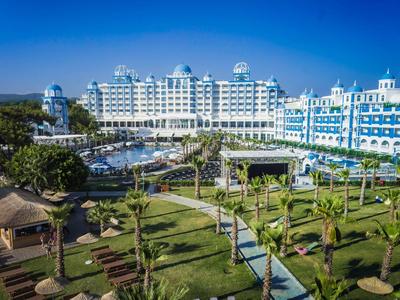 Plage courbée avec chaises longues et parasols, jetée s'étendant dans une mer turquoise.