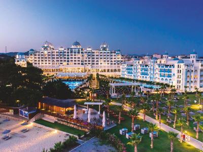 Hôtel luxueux avec piscine et jardins éclairés en soirée.