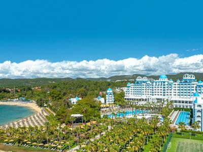 Grande complesso alberghiero con piscina, palme e spiaggia sotto il cielo azzurro.