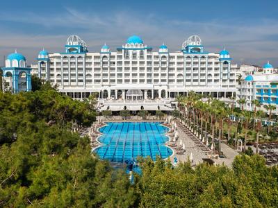 Großes Ferienhotel mit blauem Pool und grüner Vegetation bei klarem Himmel.