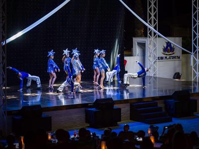 Gruppo di ballerini in costumi blu con cappelli a forma di stella che si esibiscono sul palco.
