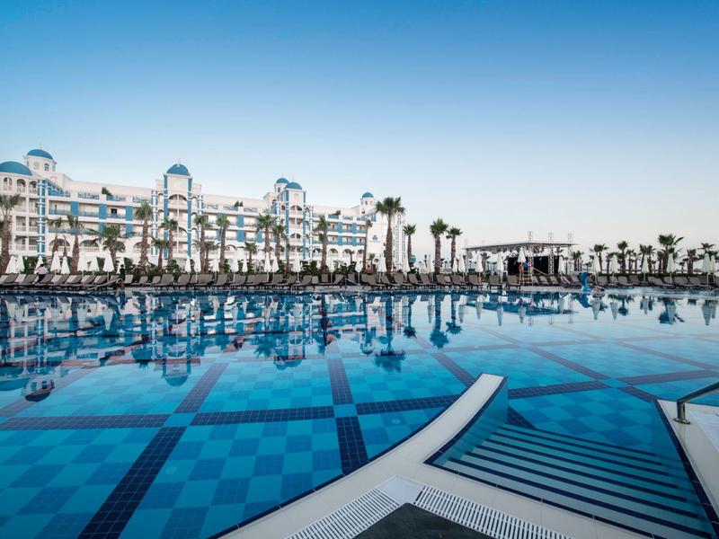Piscine à débordement devant un hôtel moderne sous un ciel bleu clair.