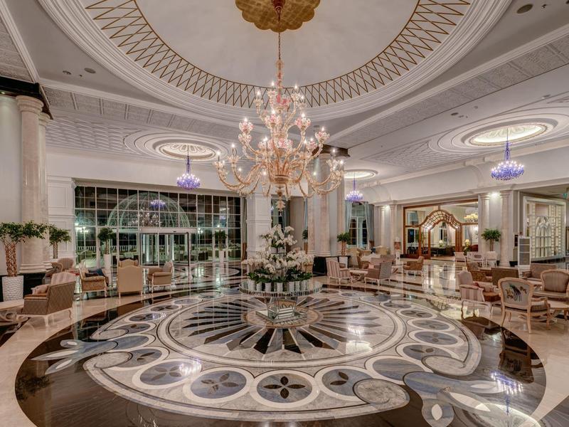 Lobby d'hôtel luxueux avec sol en marbre, lustre et fauteuils élégants.