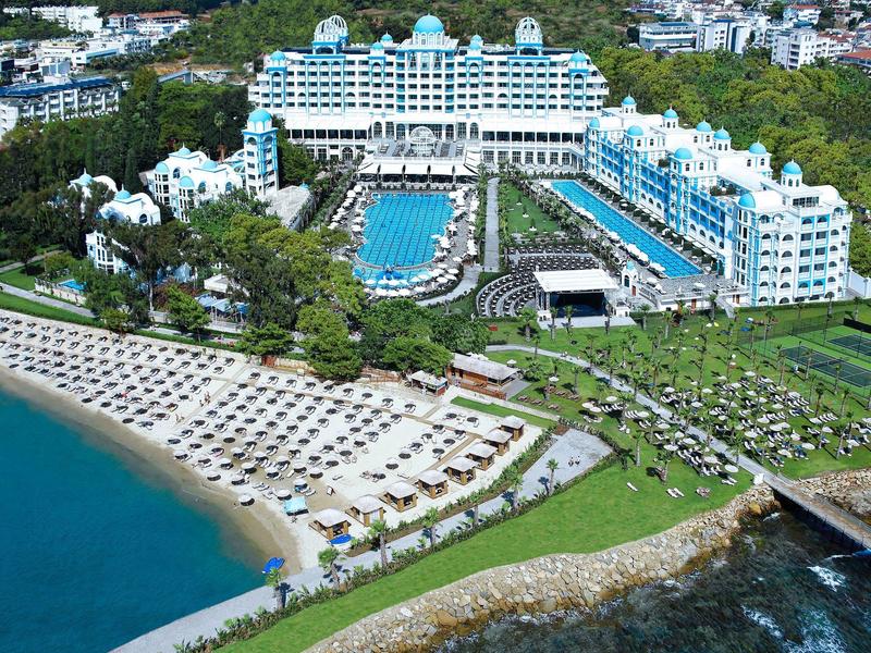 Grand hôtel blanc avec piscine, plage et chaises longues au bord de la mer.
