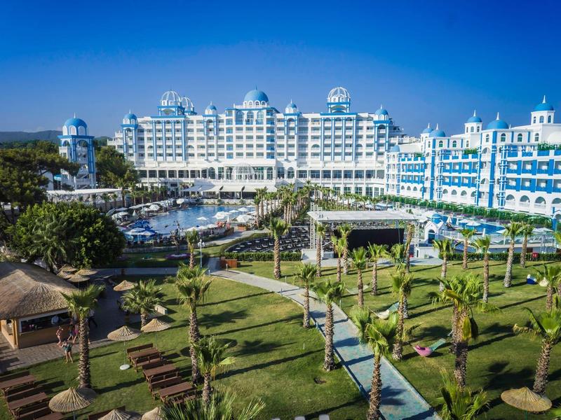 Plage courbée avec chaises longues et parasols, jetée s'étendant dans une mer turquoise.