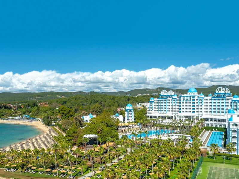 Hôtel en bord de mer avec piscines, plage, palmiers et ciel bleu clair.