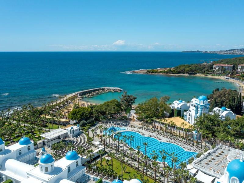 Vue d'un complexe hôtelier avec piscines, palmiers et plage au bord de la mer bleue claire.
