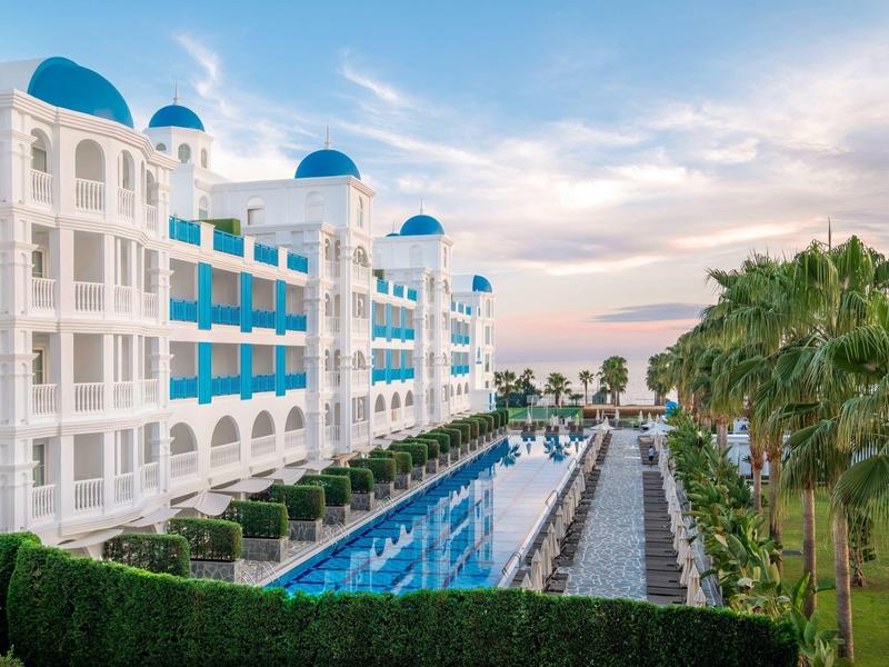 Hôtel de luxe avec bâtiments blancs et bleus à côté d'une longue piscine et des palmiers au coucher du soleil