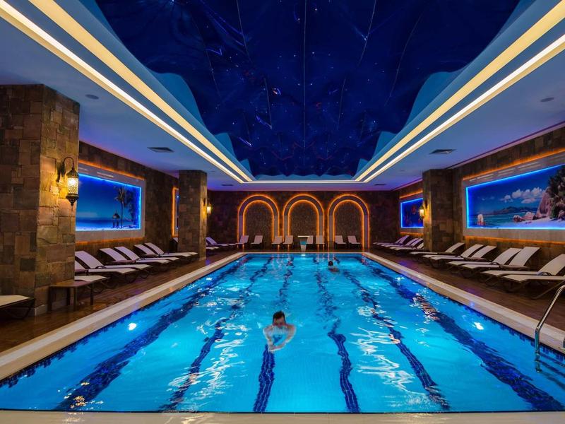 Osvětlený krytý bazén s plavci a pohodlnými lehátky v luxusním prostředí.
