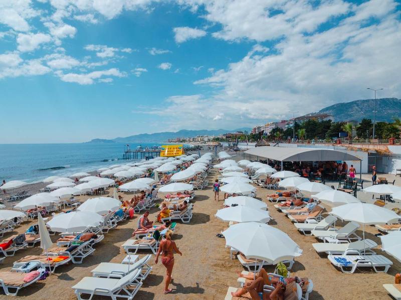 Pláž s mnoha lehátky a bílými slunečníky u moře pod modrou oblohou.