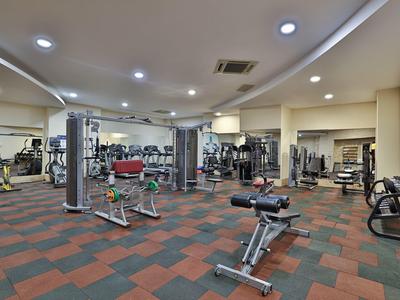 Großer Fitnessraum mit Kardiogeräten und Hanteln, heller Beleuchtung und rotem Bodenbelag.