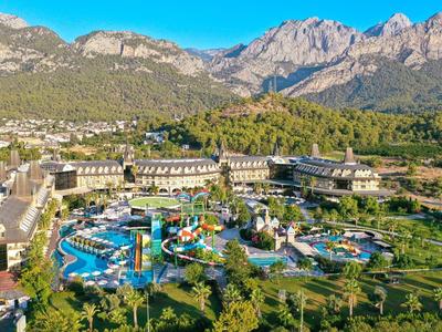 Großes Resort mit Wasserpark, grünen Bäumen und Bergen im Hintergrund unter blauem Himmel.