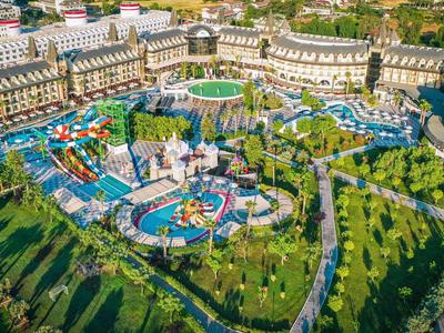 Großer Freizeitpark mit bunten Fahrgeschäften, Wasserbereichen und viel Grünfläche im Tageslicht.