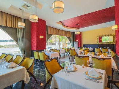 Innenraum eines Restaurants mit gelben Stühlen, weißen Tischtüchern und großen Fenstern mit Vorhängen.