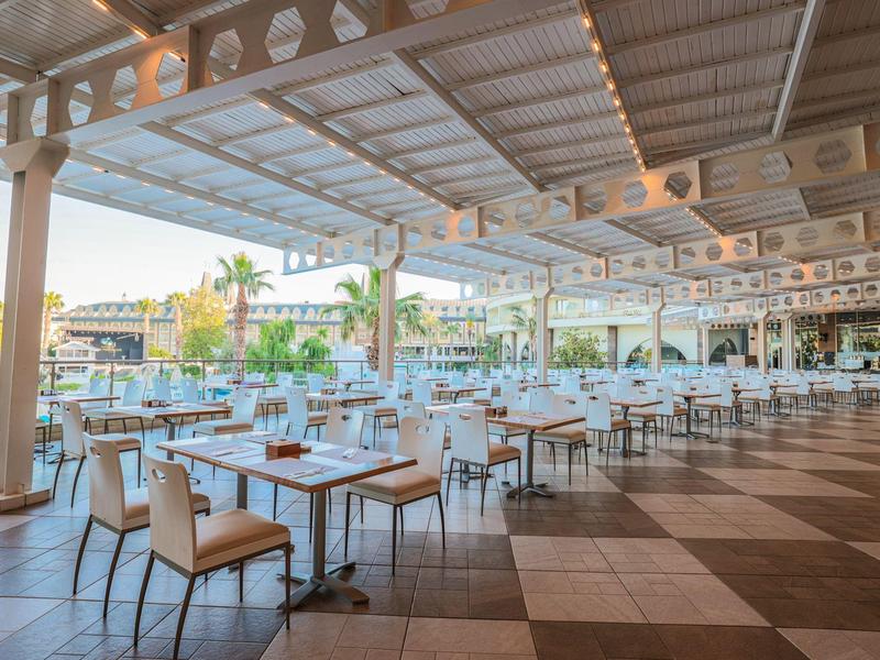 Restaurante al aire libre con mesas y sillas bajo una estructura cubierta durante el día.