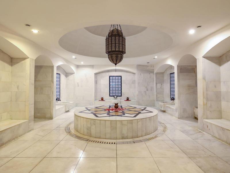 Un elegante hamam con piscina de mármol y bancos empotrados en tonos crema.