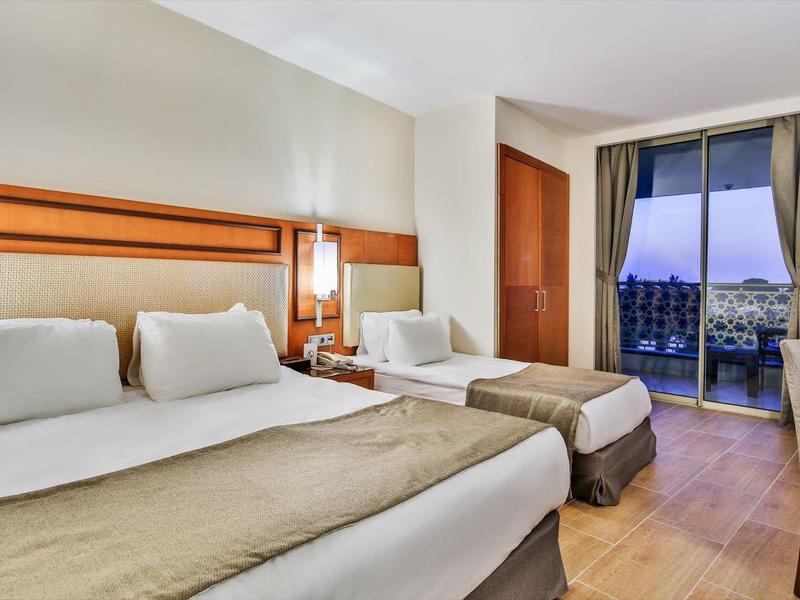 Habitación de hotel moderna con dos camas dobles, área de estar y balcón con vista al mar al atardecer.