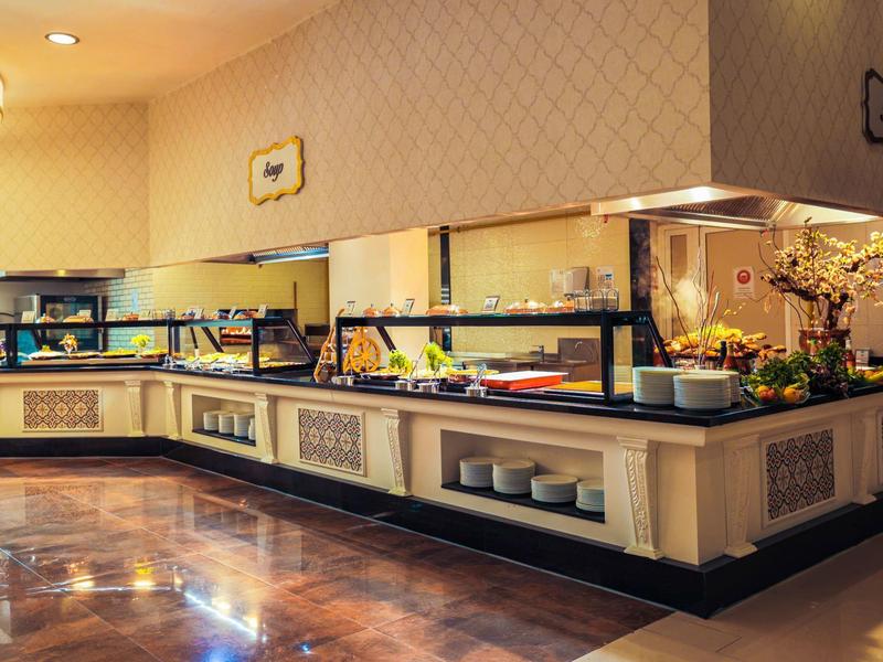 Área de buffet con luces cálidas, paredes de vidrio y flores decorativas en un restaurante de hotel.