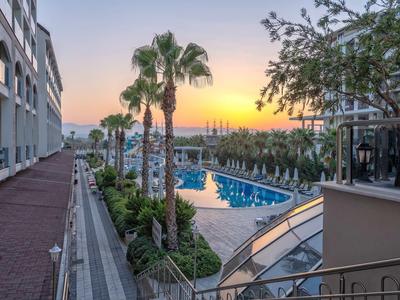 Vista serale di un hotel con piscina e palme sotto un cielo arancione.