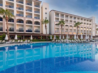 Moderní hotelový komplex s velkým venkovním bazénem a palmami za slunečného počasí