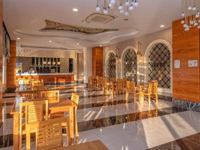 Světlá hotelová restaurace s dřevěným nábytkem, mramorovou podlahou a velkým barem v pozadí.