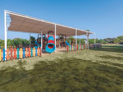 Hřiště s barevným lezeckým rámem a skluzavkou pod slunečním přístřeškem v exteriéru.