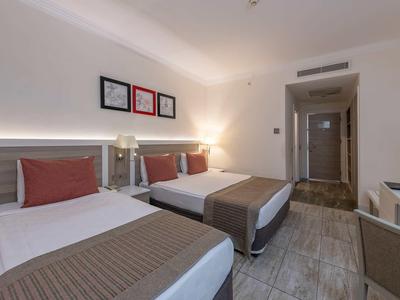 Moderní hotelový pokoj se dvěma postelemi, šedou podlahou a neutrální výzdobou stěn.