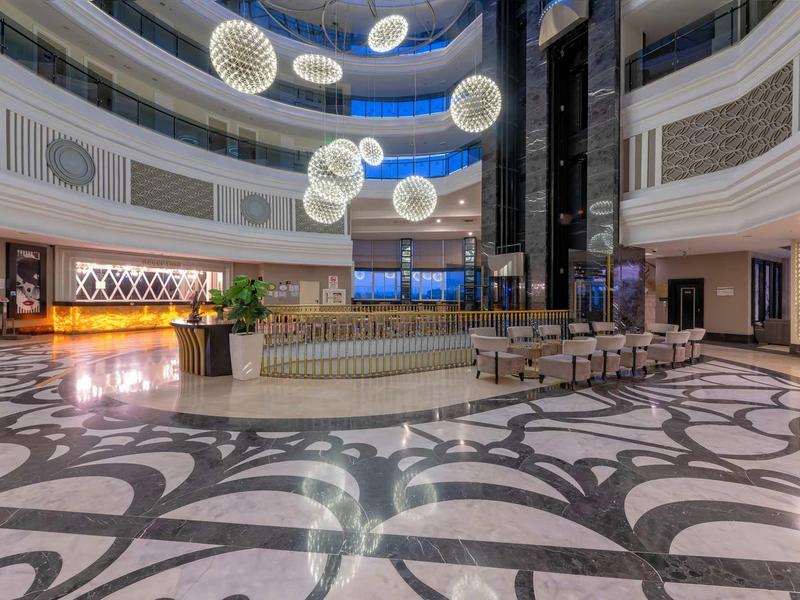 Prostorná elegantní hotelová lobby s kulatými závěsnými světly a vzorovanou podlahou.