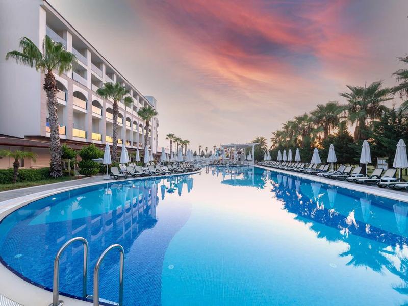 Velký hotelový bazén s lehátky a palmami při západu slunce.