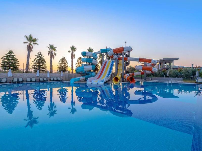 Vodní park s tobogány a bazénem pod čistou oblohou při západu slunce.