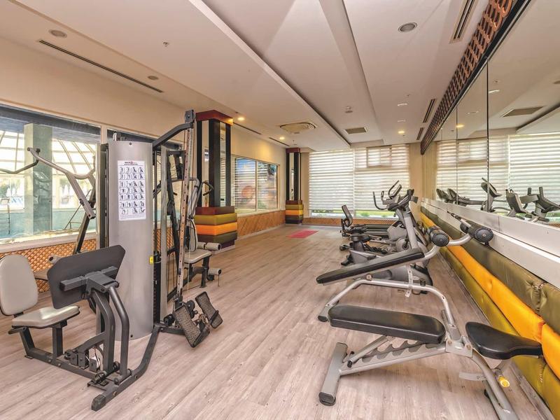 Světle hotelové fitness s různými posilovacími stroji a velkými zrcadly.