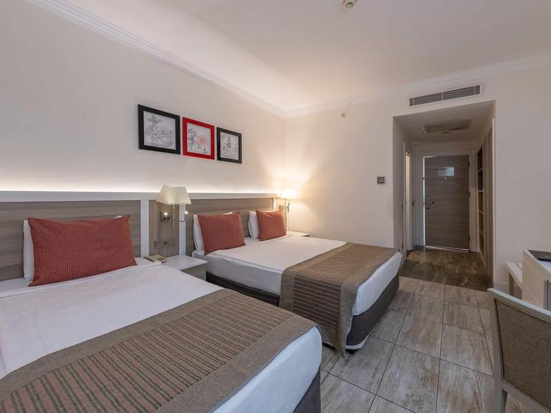 Moderní hotelový pokoj se dvěma postelemi, šedou podlahou a neutrální výzdobou stěn.