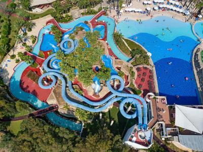 Großer Wasserpark mit blauen Rutschen, mehreren Becken und vielen grünen Bäumen.