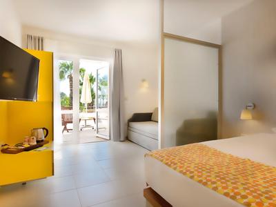 Modernes Hotelzimmer mit Bett, gelbem TV-Möbel, Terrasse und hellen Wänden.