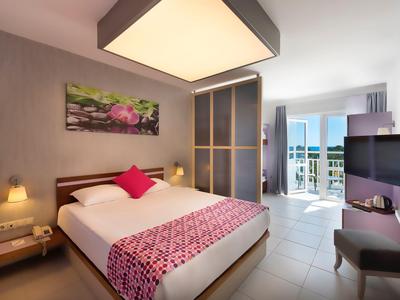 Modernes Hotelzimmer mit Doppelbett, großem Fenster, Balkon und Meerblick am hellen Tag.