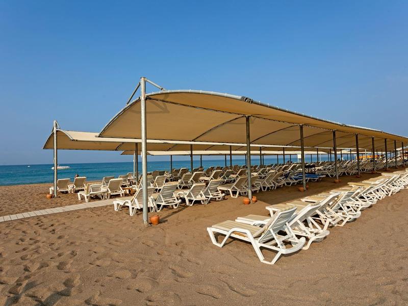 Slunečník a lehátka řadně uspořádána na písečné pláži pod jasně modrou oblohou.
