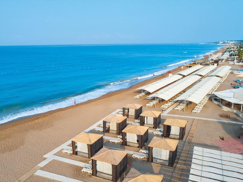 Pláž s deštníky a lehátky podél klidného modrého moře pod jasnou oblohou.