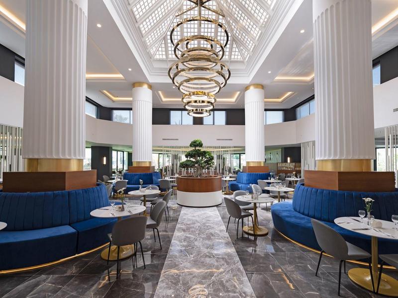 Luxusní hotelová hala s modkým sezením, velkými sloupy a elegantními lustry.